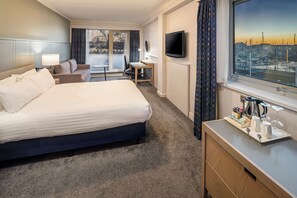 Habitación de hotel con cama, escritorio, televisor y ventana con vista a la ciudad.