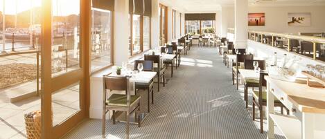 Un comedor amplio con mesas y sillas largas, ventanas grandes y vistas al exterior.