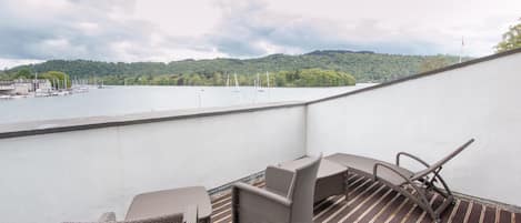 A balcony with wicker furniture and a view of a lake and hills.