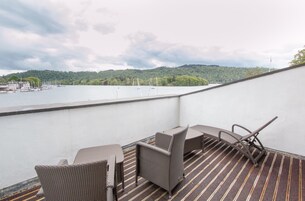 Un balcón con mobiliario de mimbre y vista a un lago y colinas.