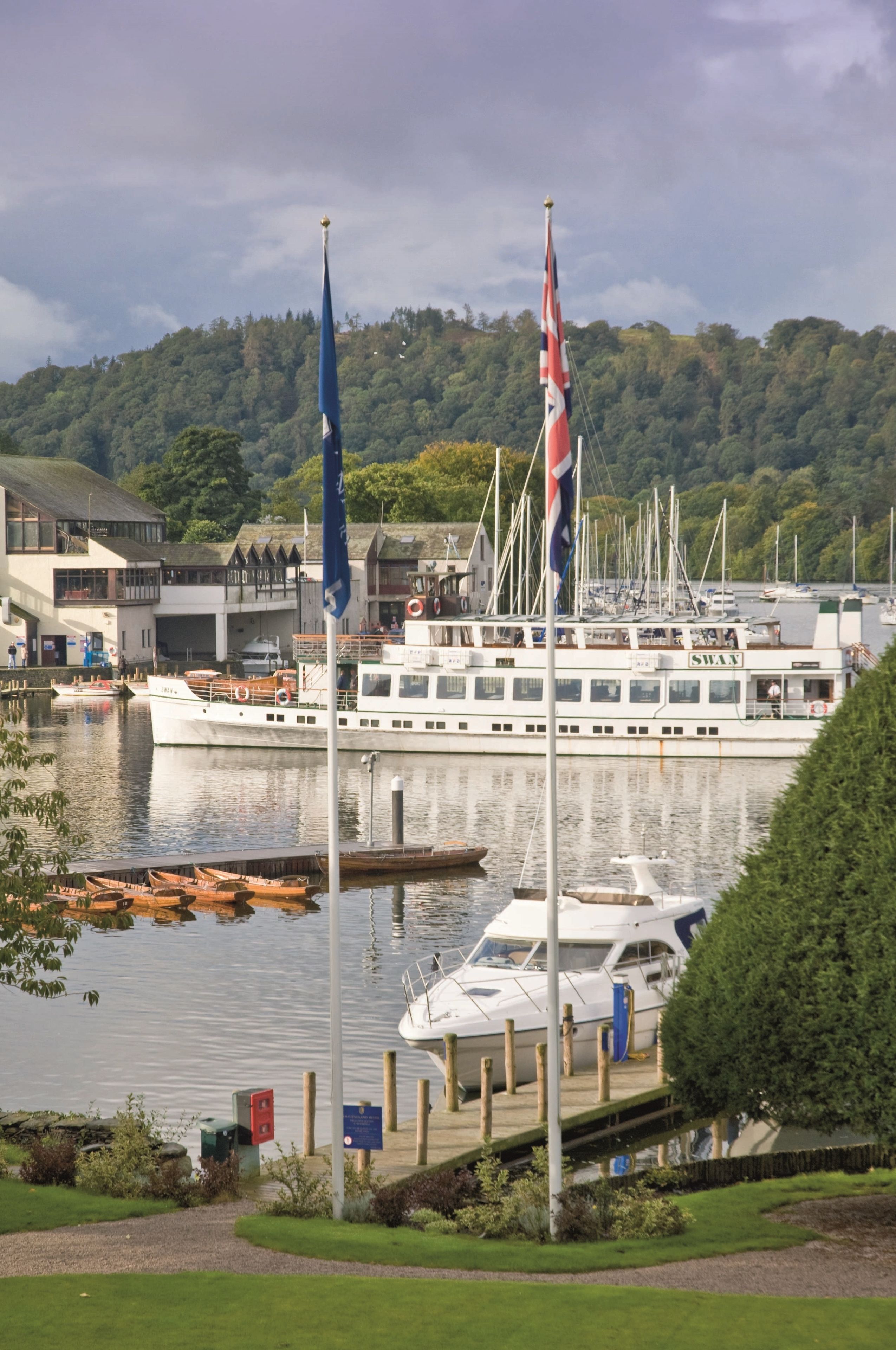Un port de plaisance où est amarré un grand bateau blanc, entouré de plus petits bateaux et d’un bâtiment sur lequel on peut lire l’inscription « SHAY ».