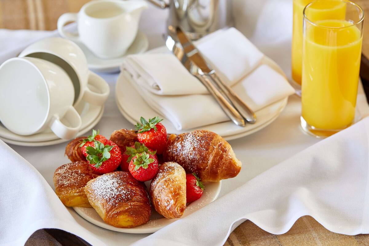 A breakfast setting with pastries, strawberries, a cup of coffee, a teapot, and a glass of orange juice.