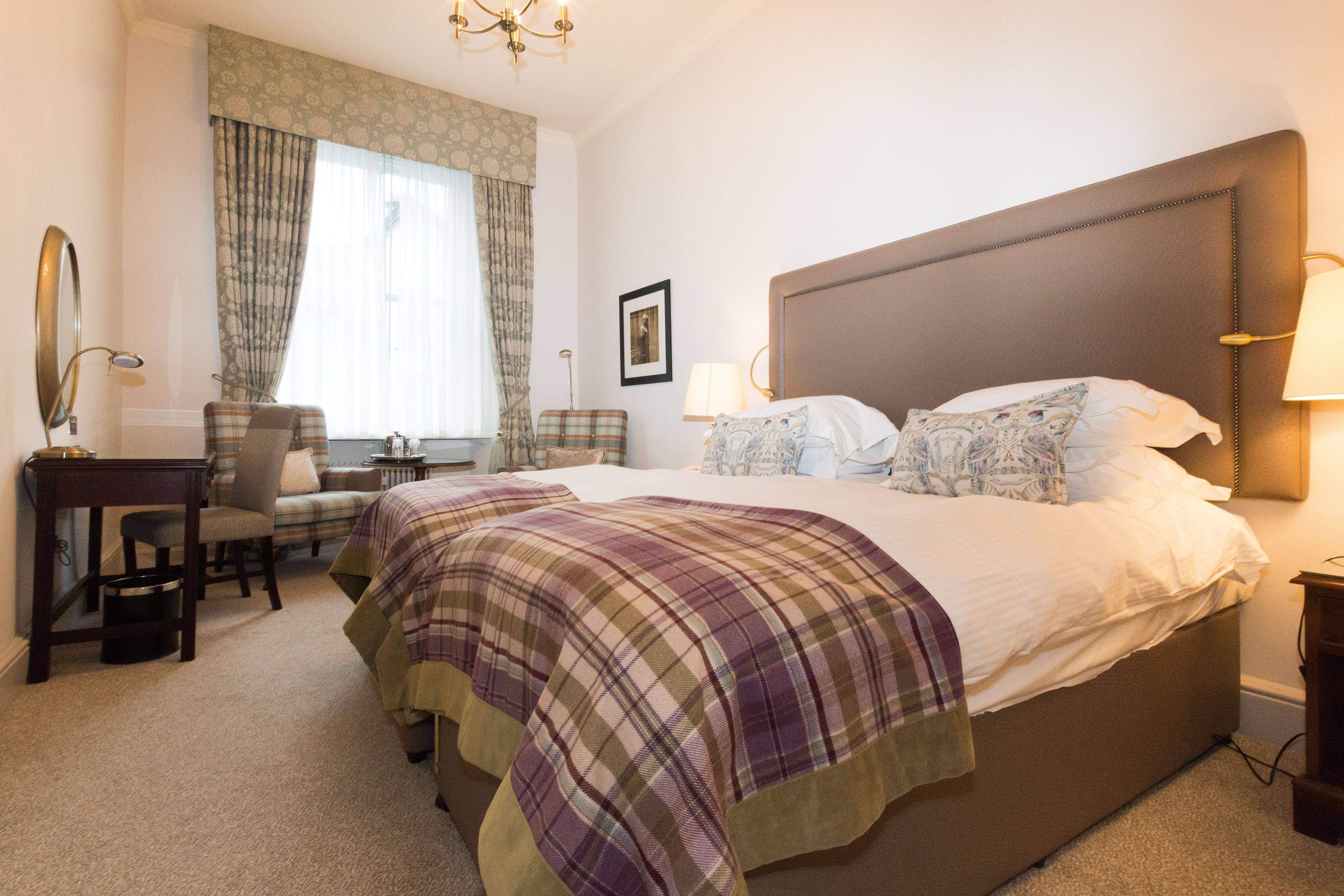 A hotel room with a large bed, a desk with a chair, a small table, and a window with curtains.