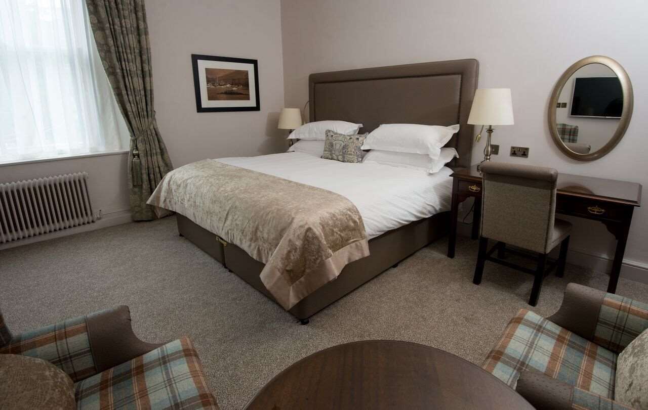 A hotel room with a large bed, two bedside tables, a chair, a round table, a mirror, and a radiator.