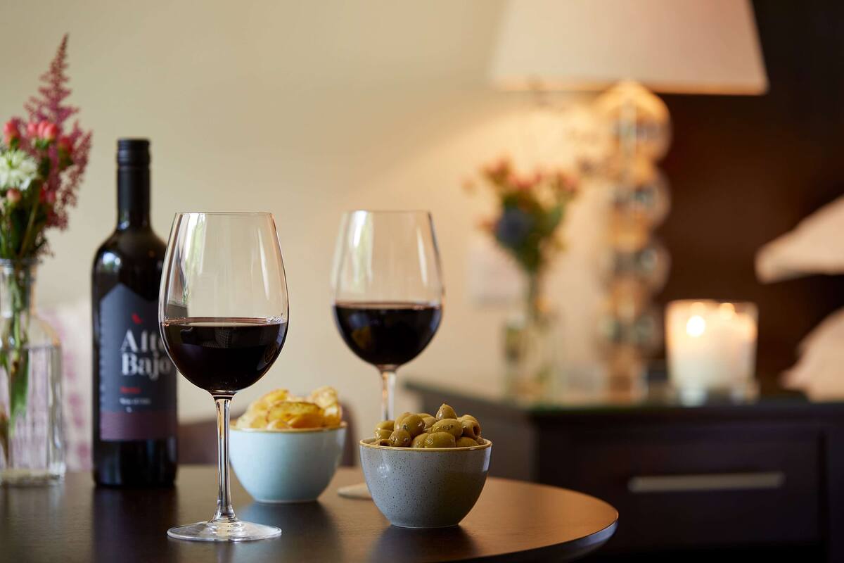 A table with two wine glasses, a bottle of wine, and bowls of olives and chips.