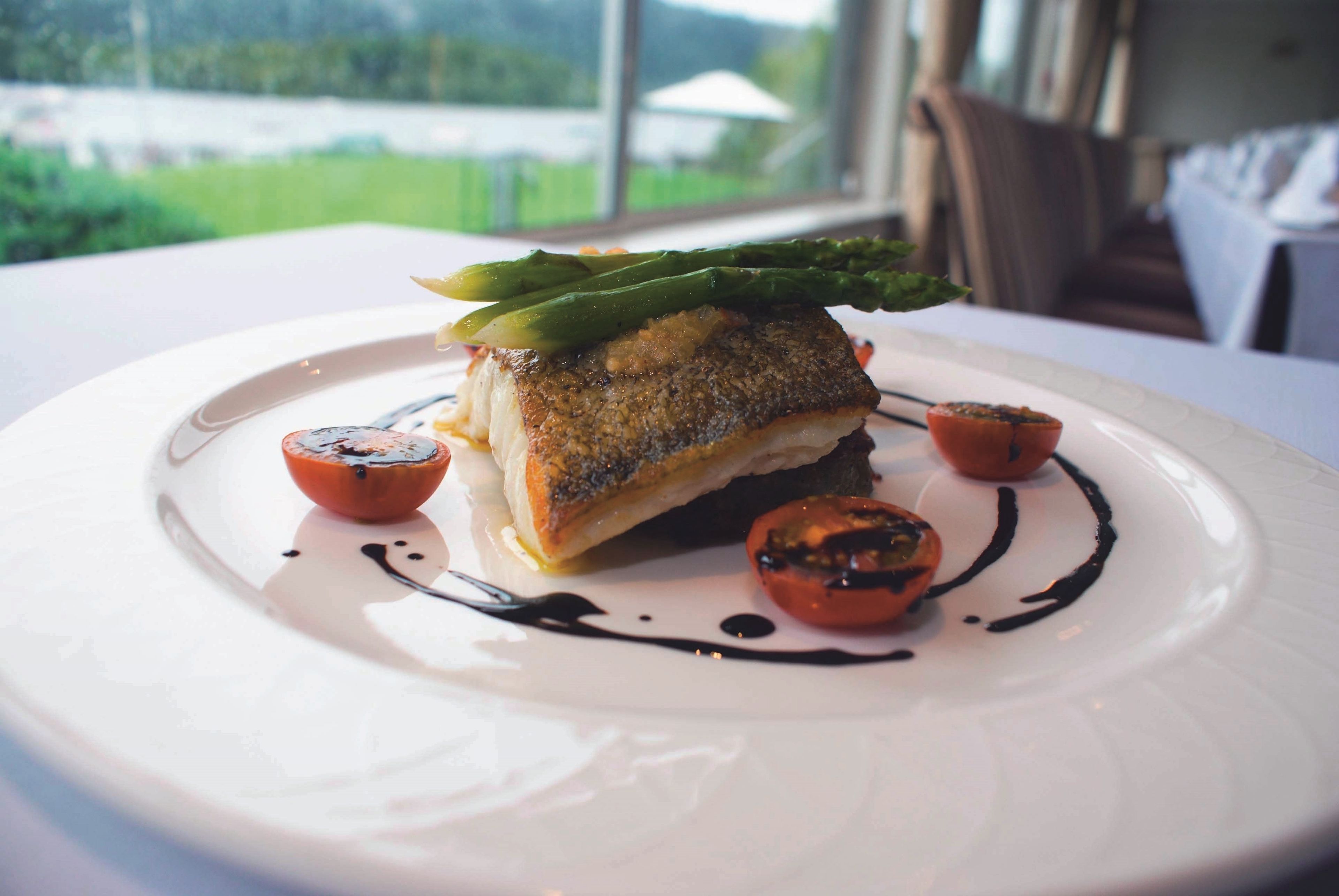 A plate of food with a fish fillet, asparagus, and small tomatoes, served on a white plate.