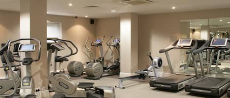 Un gimnasio con diversas máquinas de cardio, incluyendo cintas de correr y elípticas, dispuesto en un espacio amplio.