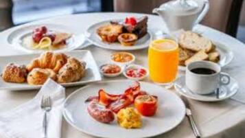 Un esmorzar preparat amb plats d'ous, salsitxes i pastissos, una gerra de suc d'aranja i una tassa de cafè.