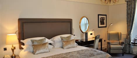 Habitación de hotel con una cama grande, una mesita de noche con lámpara, una silla, un espejo y un candelabro.