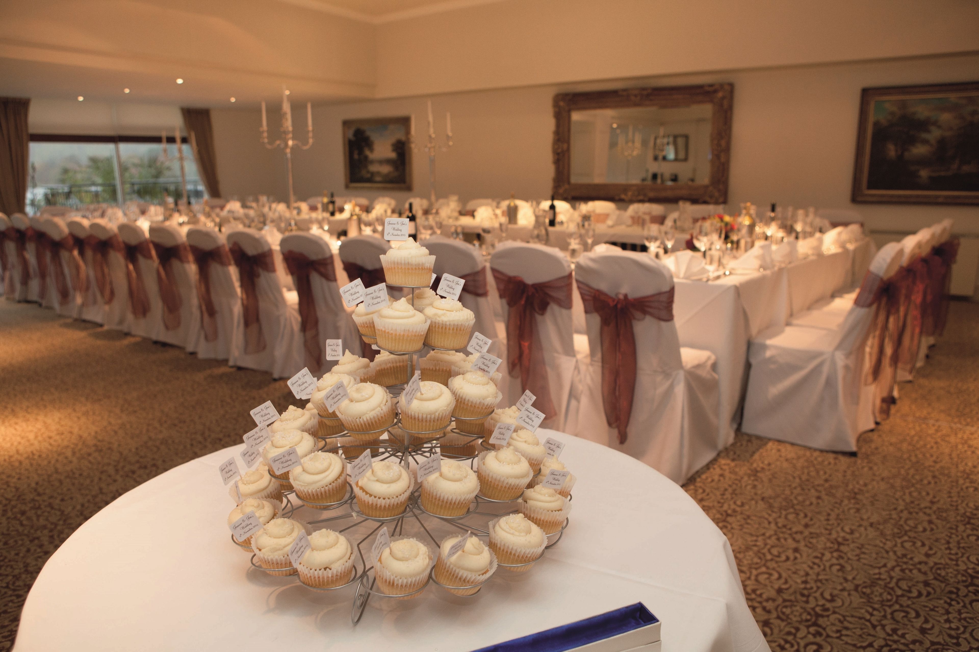 A banquet hall with round tables set for a formal event, featuring a tiered cupcake display in the foreground.