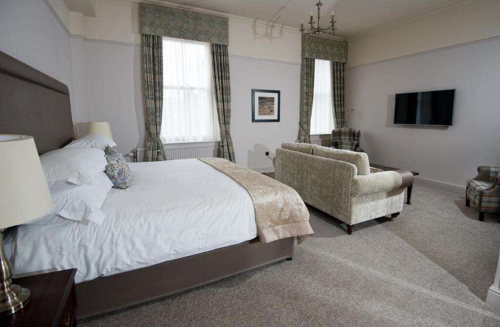 A bedroom with a large bed, a sofa, a television, and a carpeted floor.