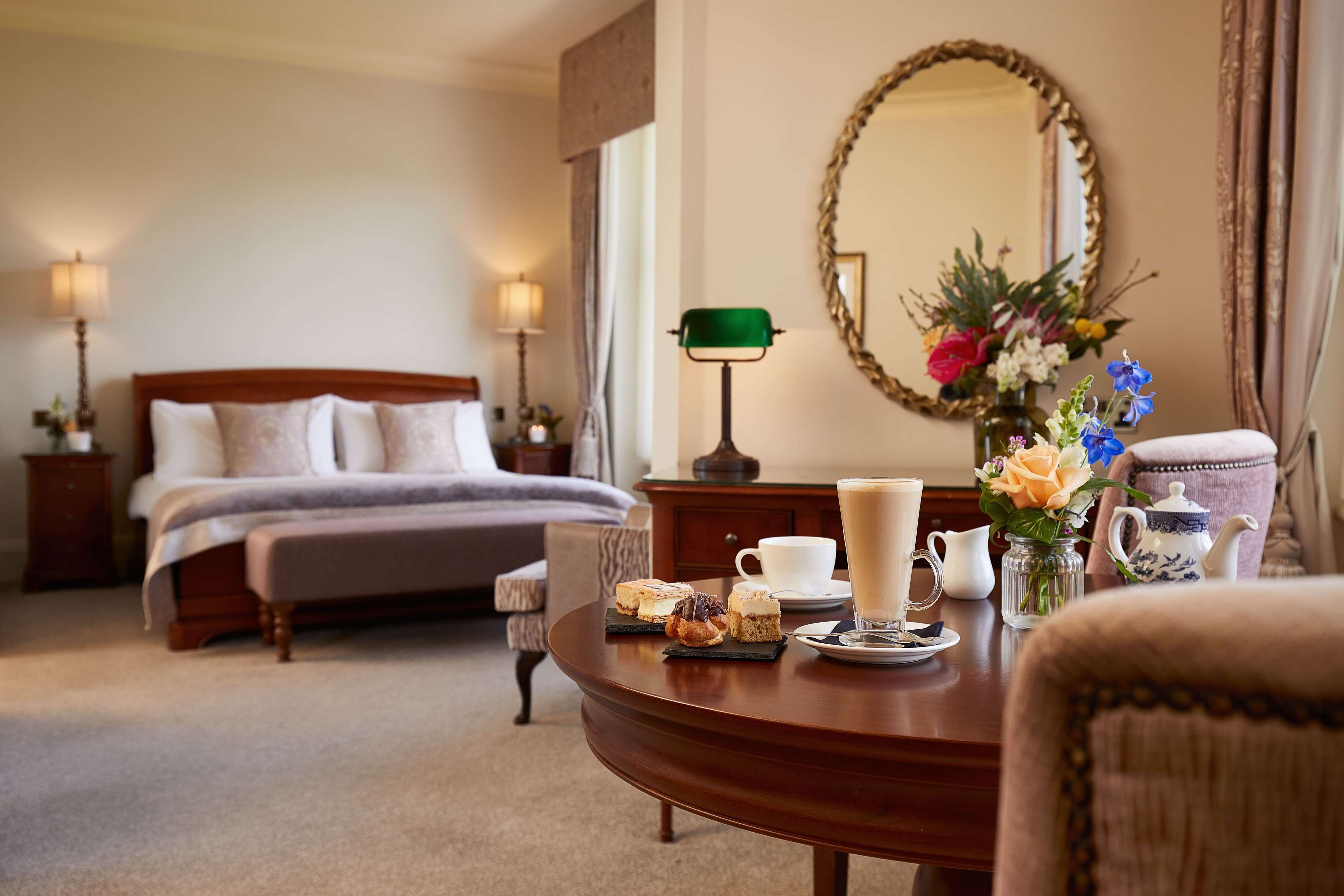 Ein Hotelzimmer mit einem Bett, Nachttischen, einem runden Tisch mit einer Tasse Kaffee, einem Teekessel und einer Blumenvase.