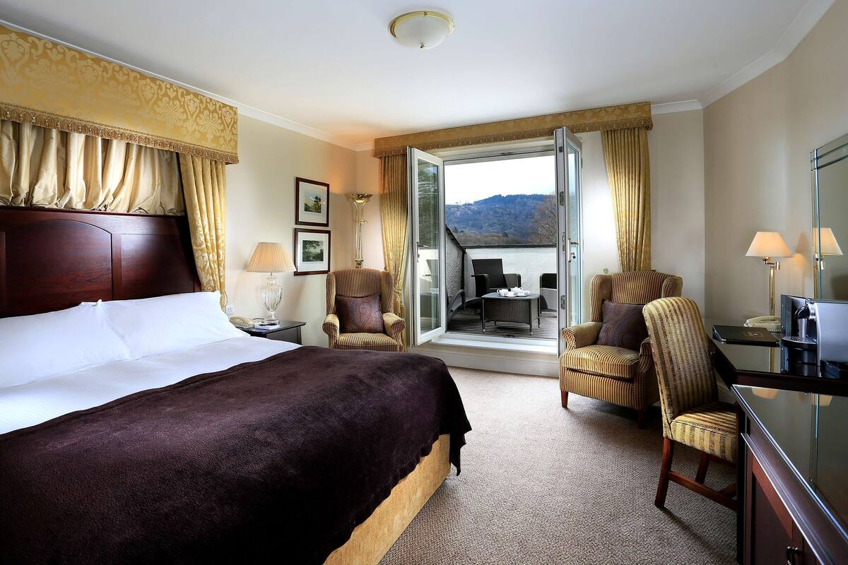 A hotel room with a large bed, two armchairs, a desk, and a view of the outdoors.