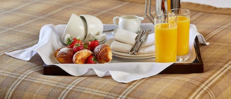 A breakfast tray with croissants, strawberries, a coffee pot, cups, and glasses of orange juice on a checkered tablecloth.