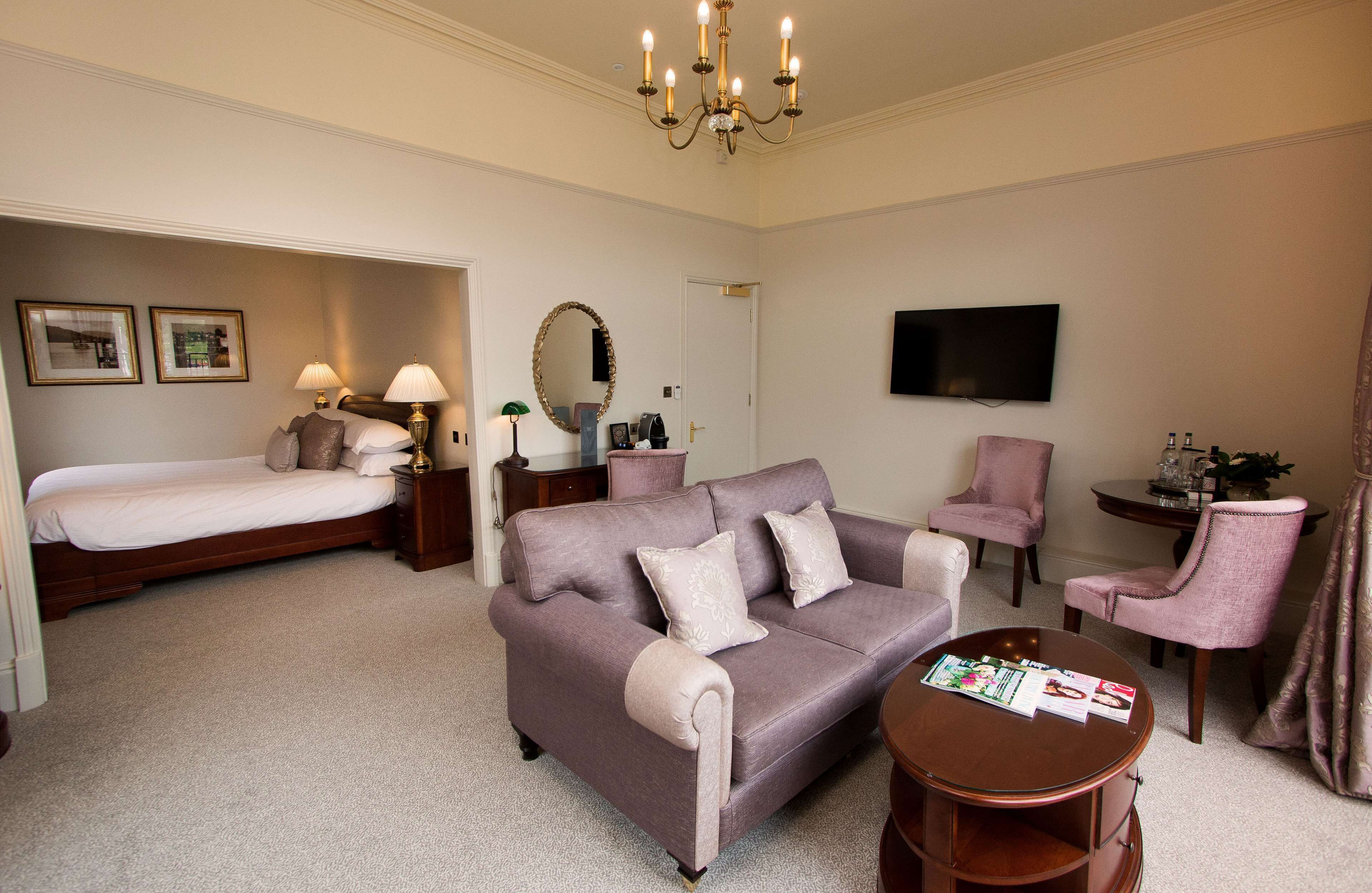 A hotel room with a bed, a sofa, a chair, a TV, and a table.