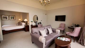 A hotel room with a bed, a sofa, a chair, a TV, and a table.