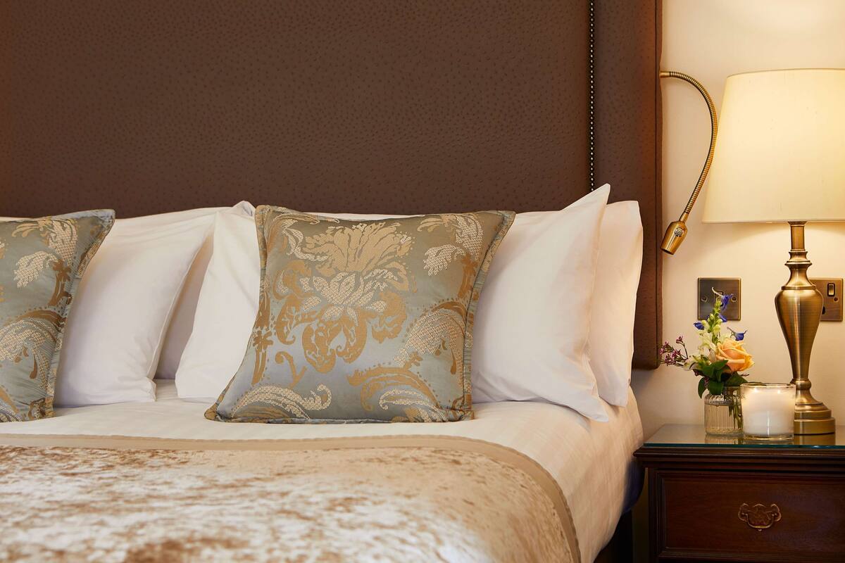 A neatly made bed with patterned pillows, a bedside table with a lamp, and a vase with flowers.