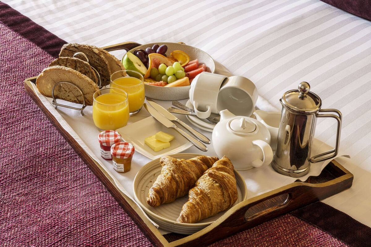 A breakfast tray with croissants, bread, fruit, juice, butter, and coffee equipment.