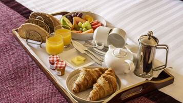 A breakfast tray with croissants, bread, fruit, juice, butter, and coffee equipment.
