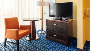 A hotel room with a television on a wooden cabinet, a round table with a lamp, and an orange chair. -  Chester Inn & Suites (Sharonville)