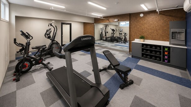 Un gimnasio con cintas de correr, bicicletas estáticas y una banca.