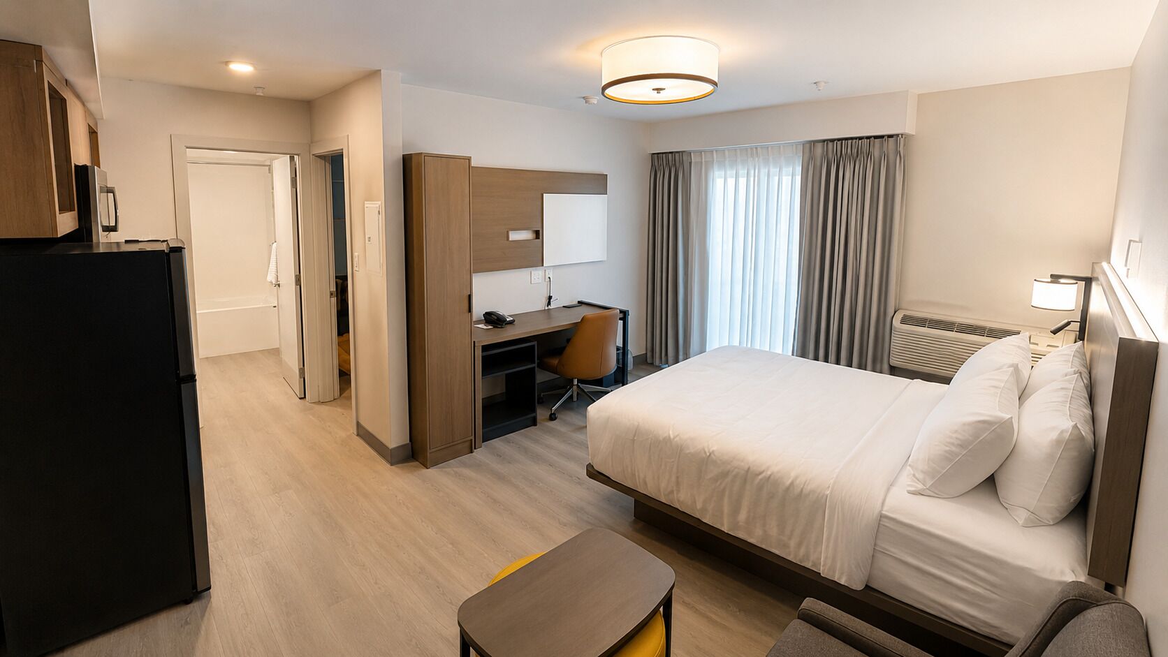 Una habitación de hotel con cama, escritorio, silla, armario y refrigerador.