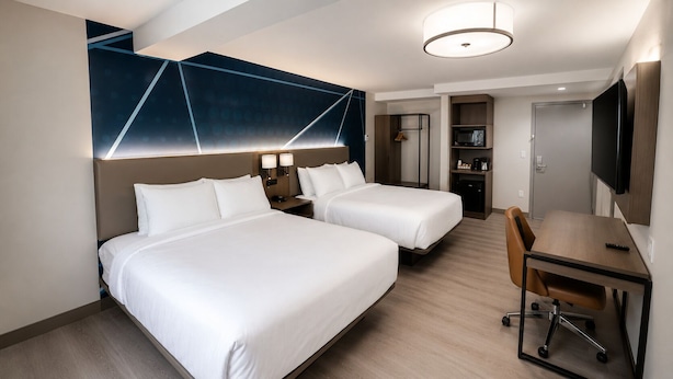 Habitación de hotel con dos camas, un escritorio, una silla, un televisor y un microondas.