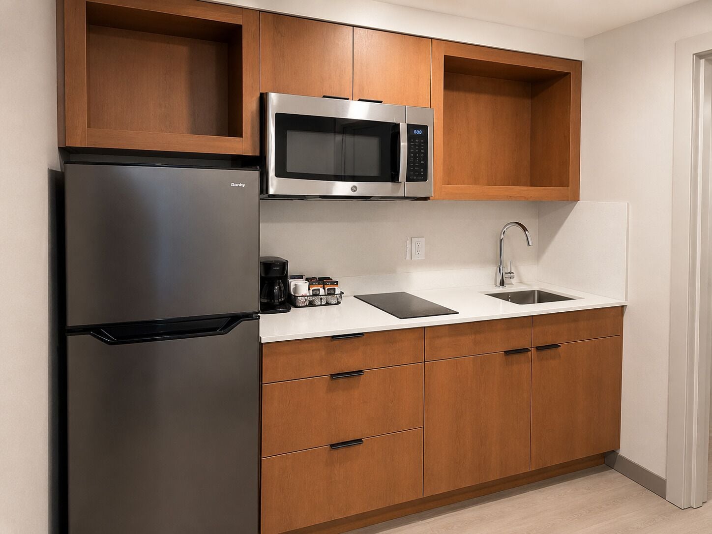 A compact kitchen with a stainless steel refrigerator, a microwave, a coffee maker, and a sink.