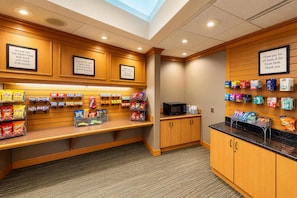 A gift shop with snack displays and a microwave. Signs direct to the front desk for purchases. - Embassy Suites Hotel Des Moines Downtown (Des Moines)