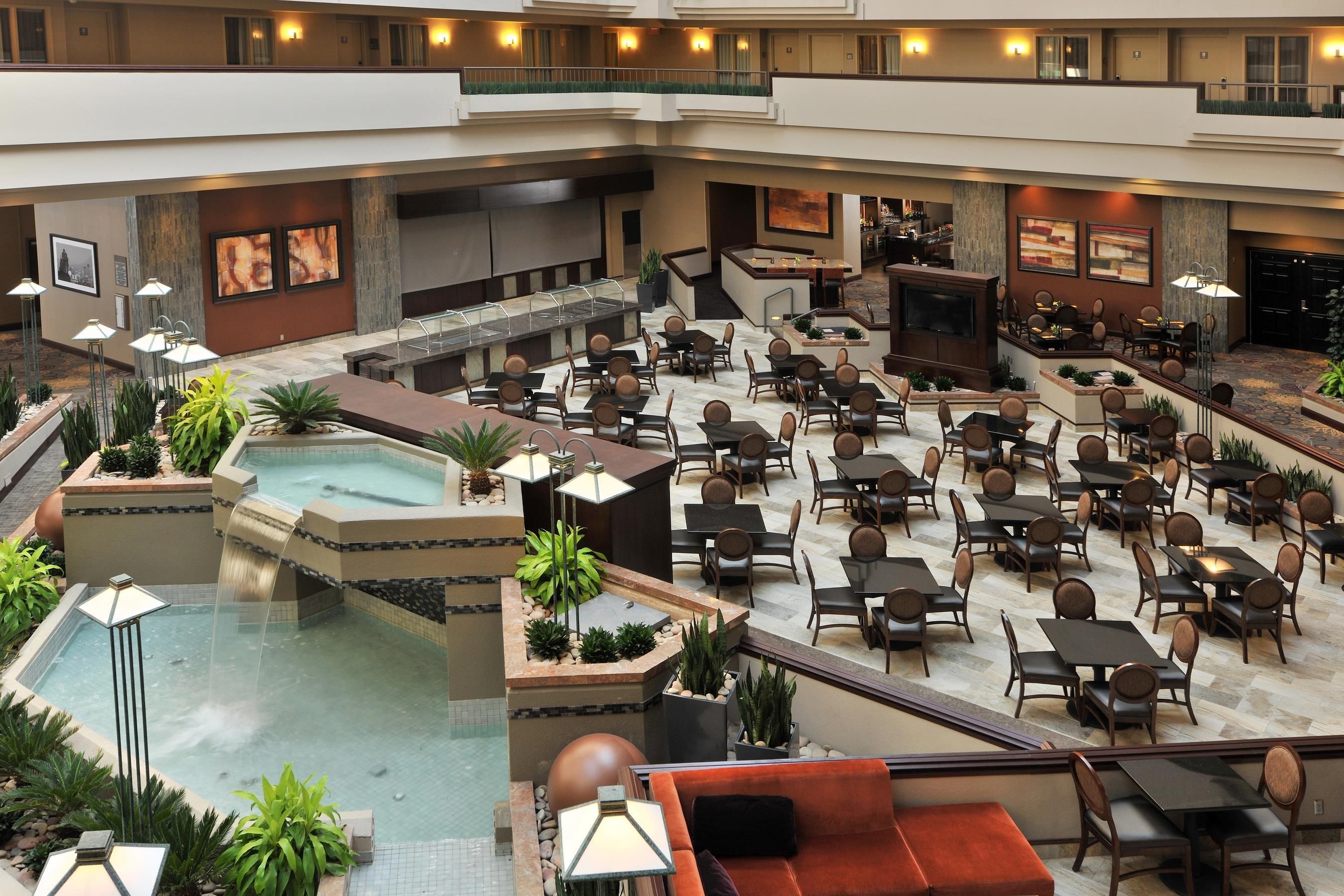 A multi-level hotel lobby with a central pool, dining area, and bar/lounge space.