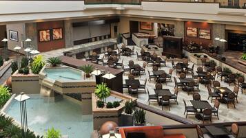 A multi-level hotel lobby with a central pool, dining area, and bar/lounge space.