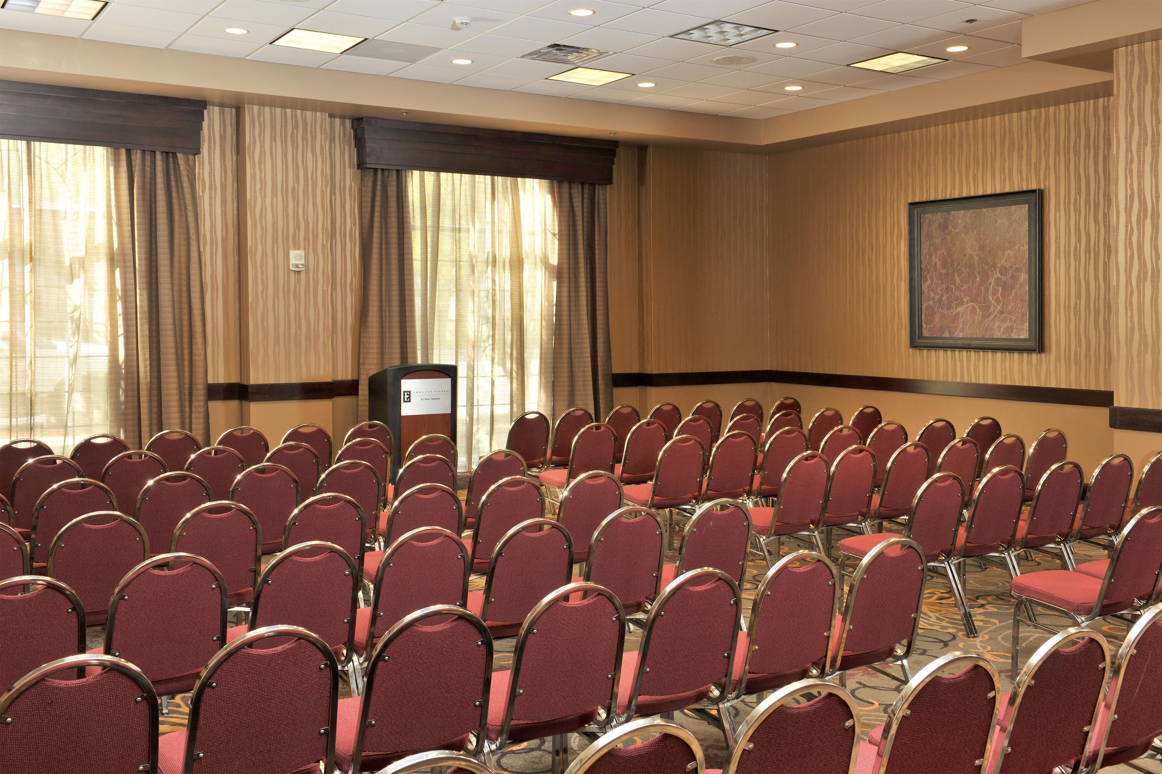 A conference room with rows of chairs, a podium, and a large window with curtains.