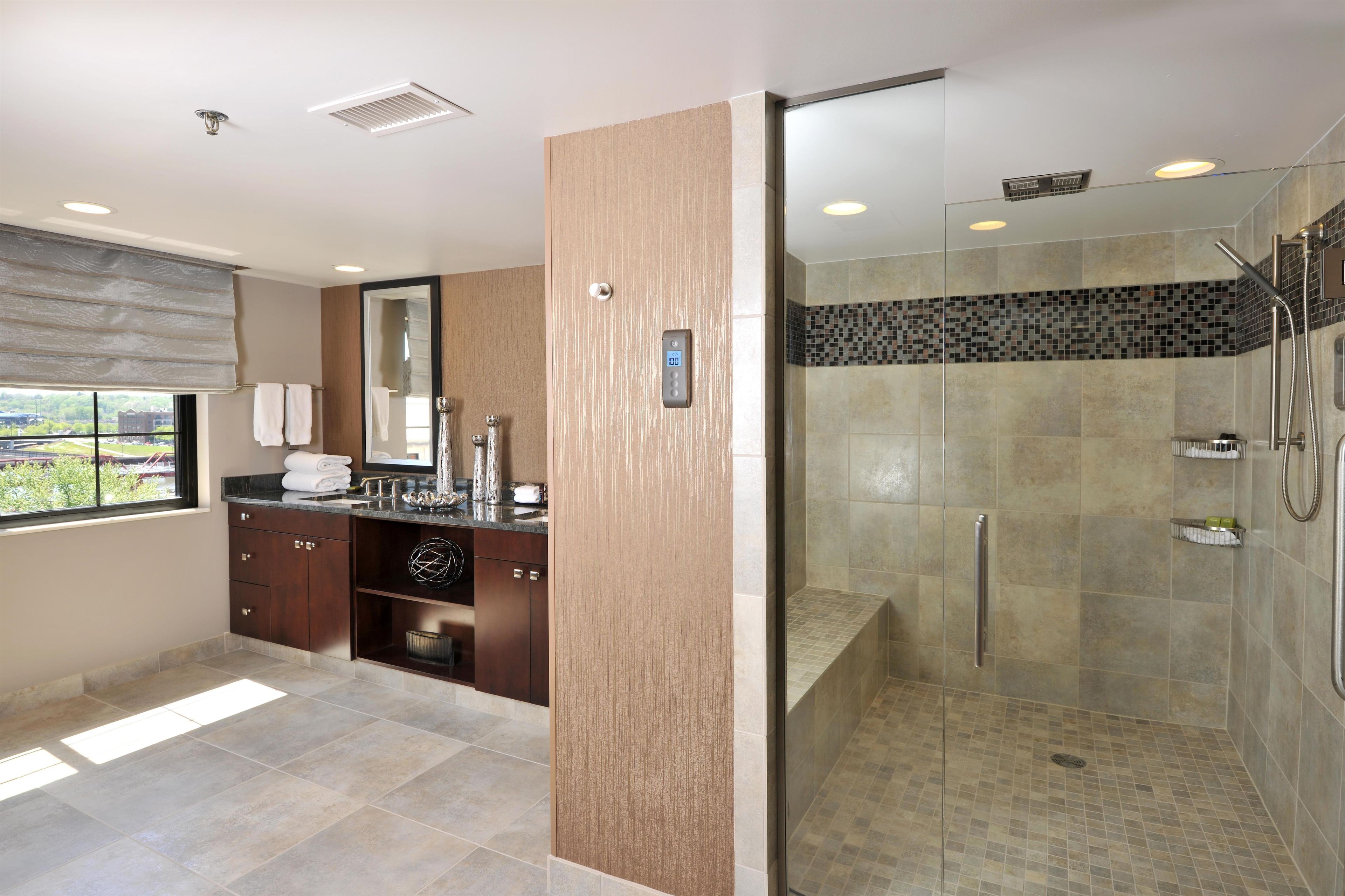 A modern bathroom with a glass-enclosed shower, a vanity with a mirror, and a window with blinds.
