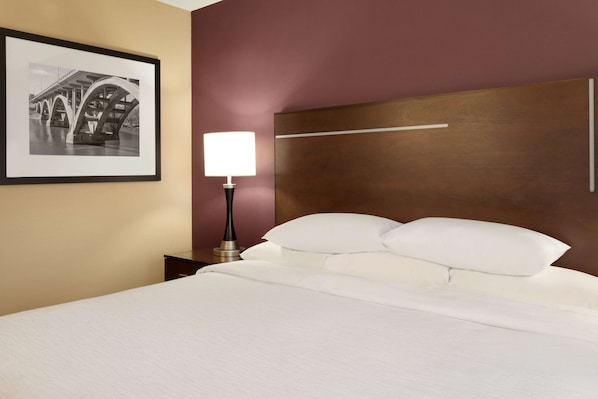 Habitación de hotel con cama, mesita de noche, lámpara, un cuadro con un puente y cabecero.