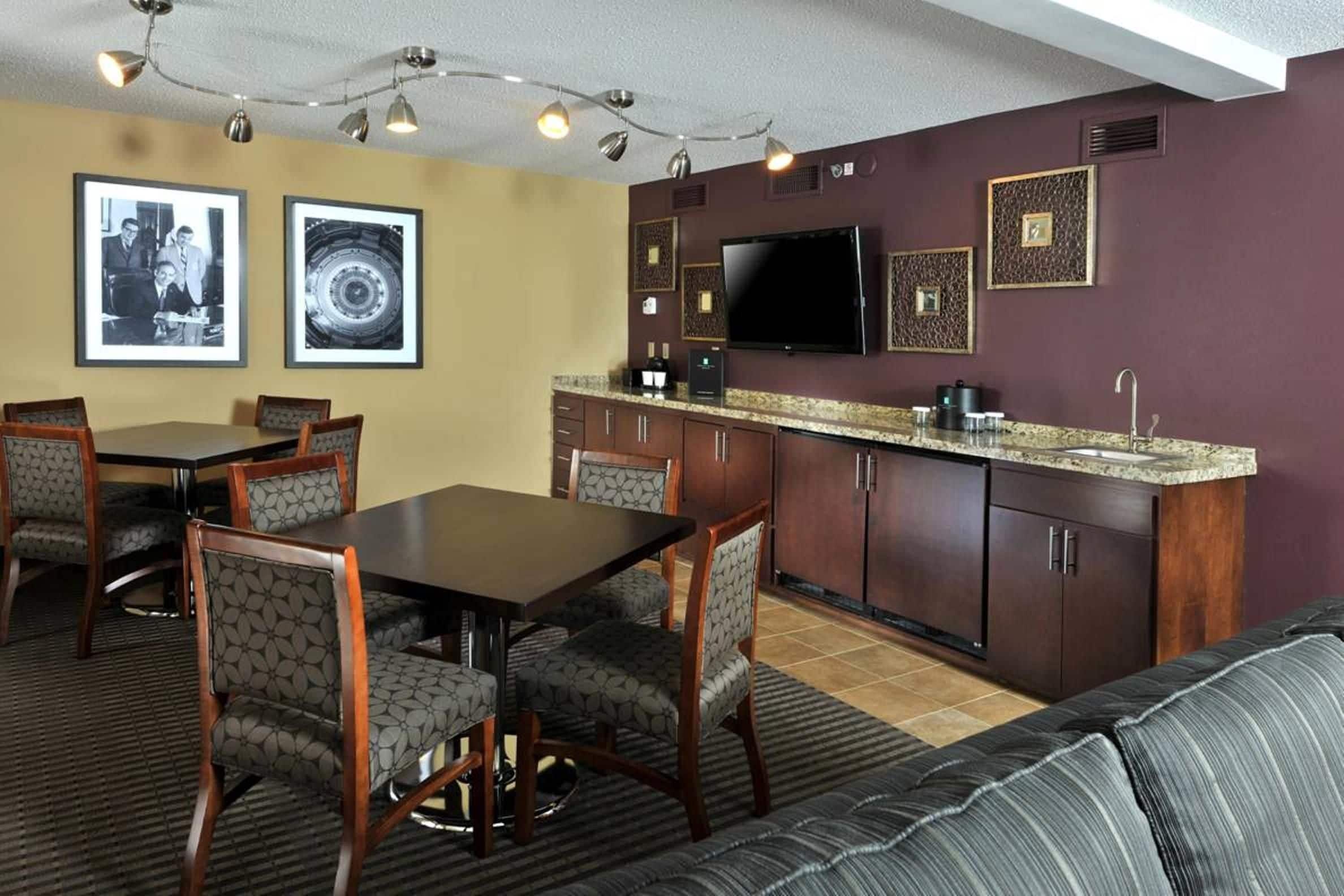 A dining area with a table and chairs, a kitchen with a TV, and framed pictures on the wall.