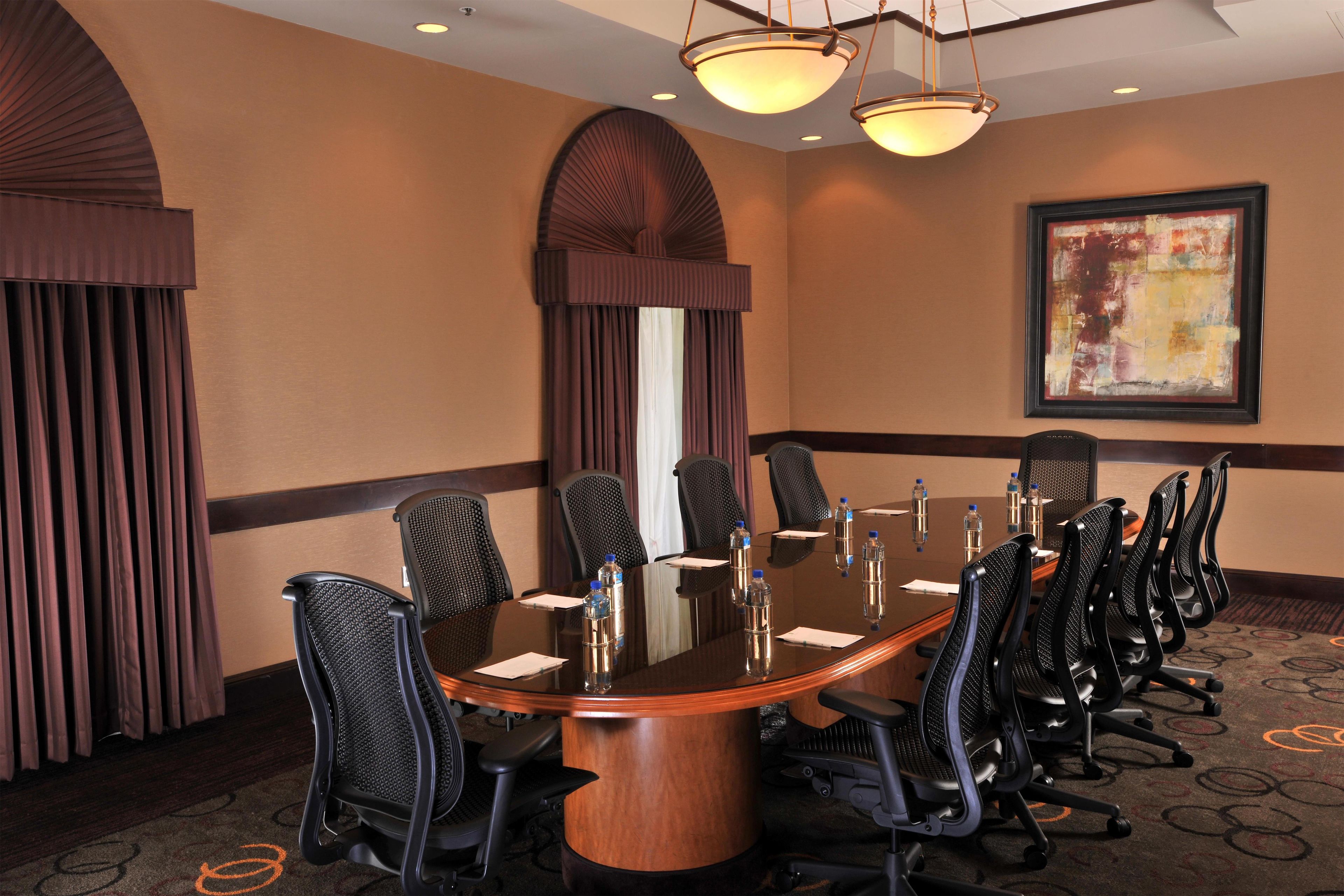 A conference room with a round table, multiple chairs, water bottles, and a framed abstract painting on the wall.