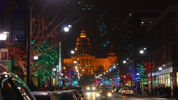 A street lined with trees decorated with colorful lights, a building with a dome, and cars on the road.