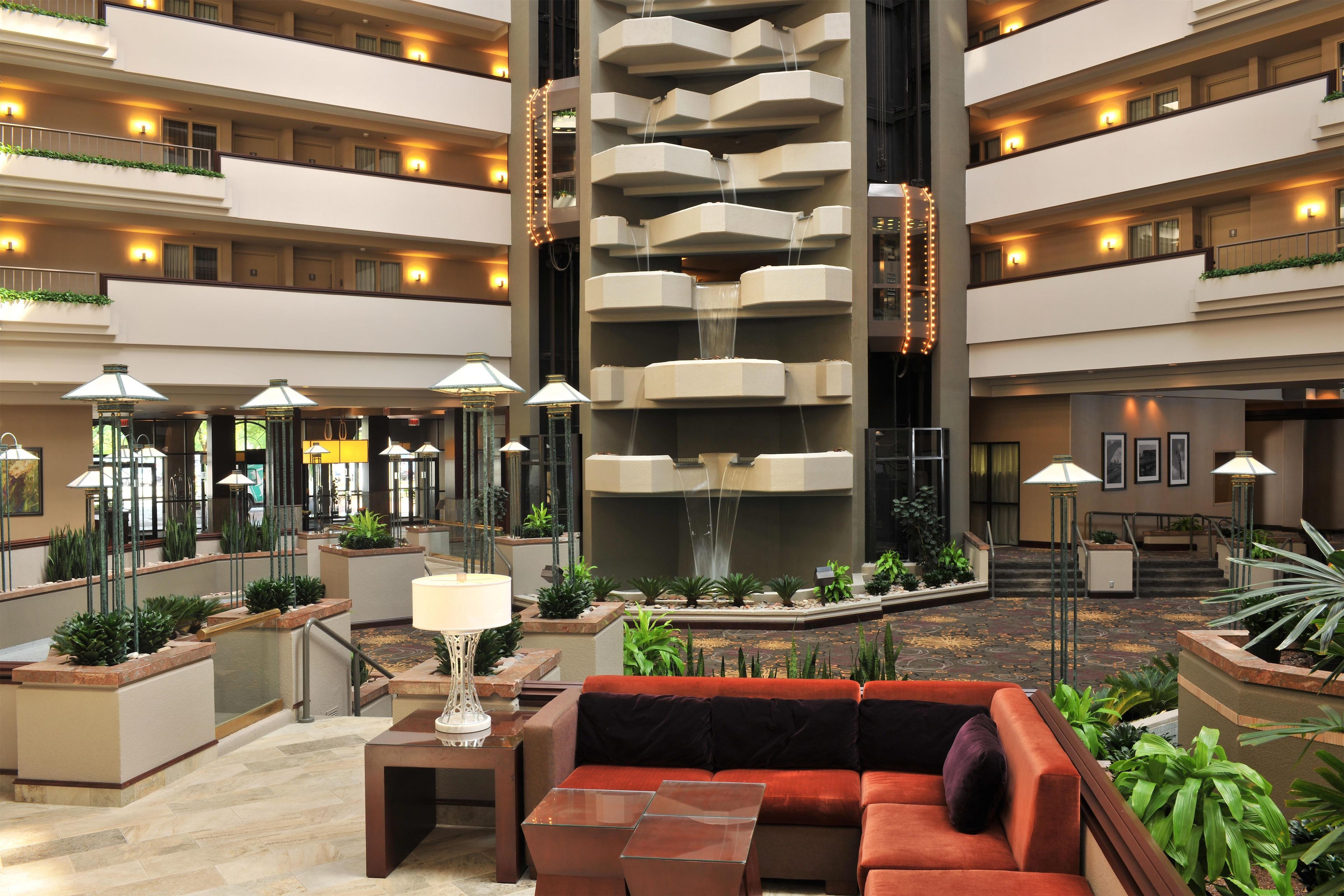 A multi-level hotel lobby with a central water feature, multiple floors, and a seating area with a sofa and table.