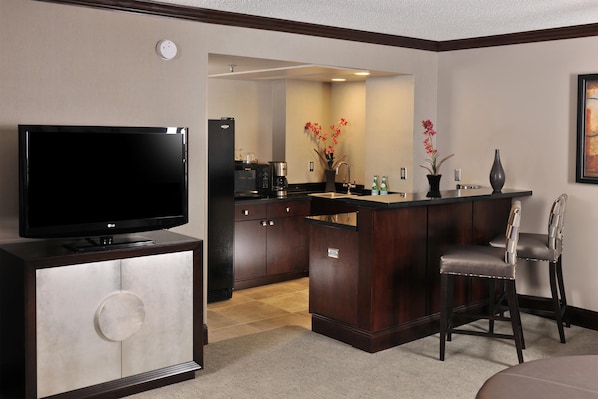 A compact living space with a flat-screen TV, a kitchenette, a dining area with a bar, and a small seating area. - Embassy Suites Hotel Des Moines Downtown (Des Moines)