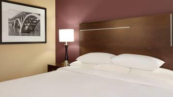 A hotel room with a bed, a nightstand, a lamp, a framed picture on the wall, and a wooden headboard.