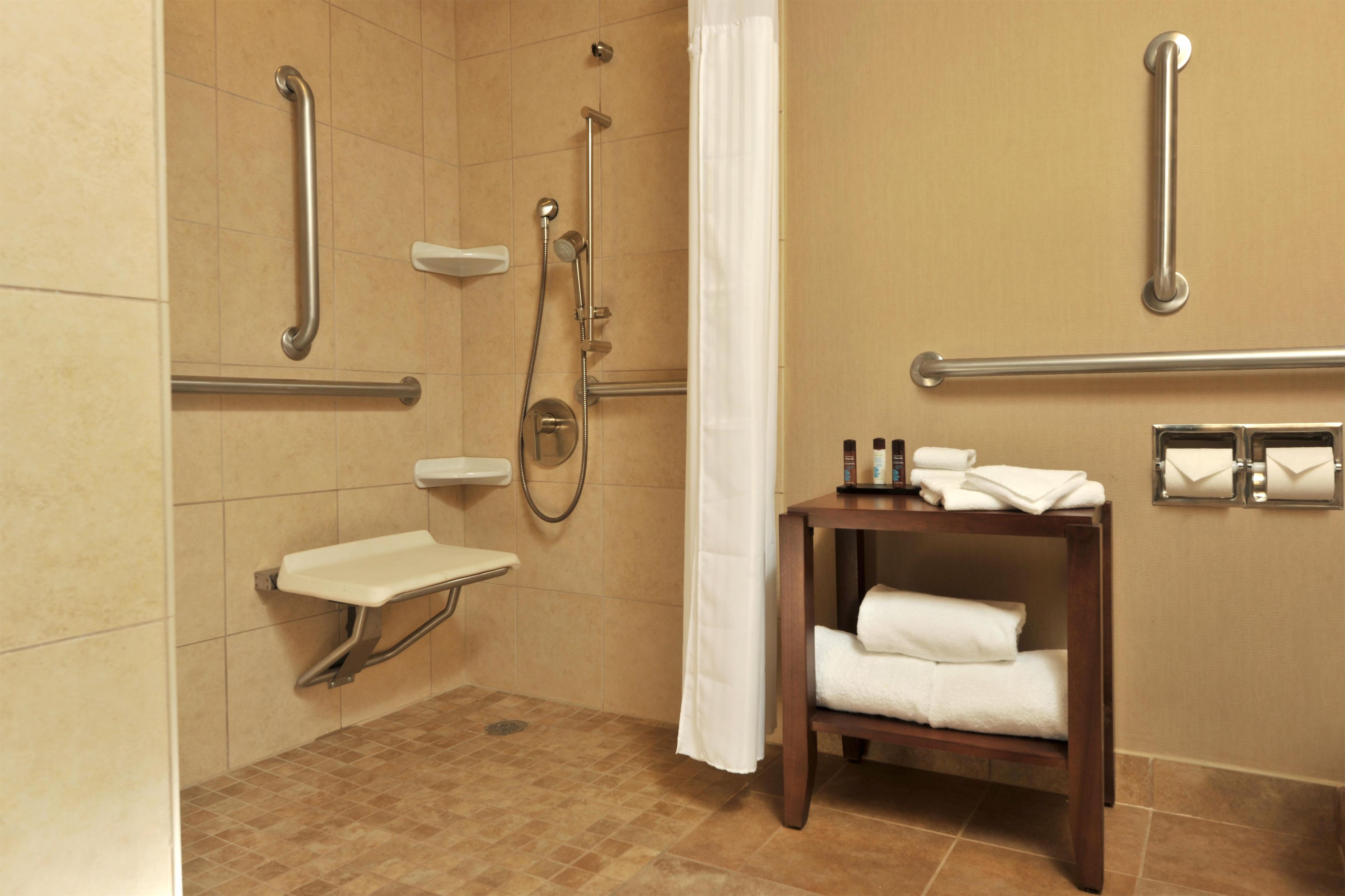 A bathroom with a shower, grab bars, a sink, and a towel rack.