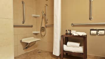 A bathroom with a shower, grab bars, a sink, and a towel rack.