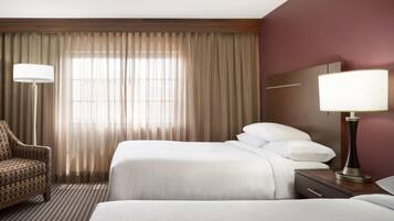 A hotel room with a bed, a chair, a bedside table with a lamp, and a window with curtains.