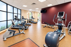 A gym with various exercise equipment, large windows, and a red accent wall. - Embassy Suites Hotel Des Moines Downtown (Des Moines)
