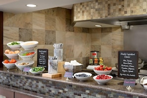 A buffet counter with various food items and condiments. - Embassy Suites Hotel Des Moines Downtown (Des Moines)