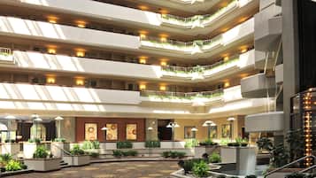 A multi-level hotel atrium with balconies, artwork, and indoor plants.