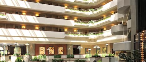 A multi-level hotel atrium with balconies, artwork, and indoor plants.