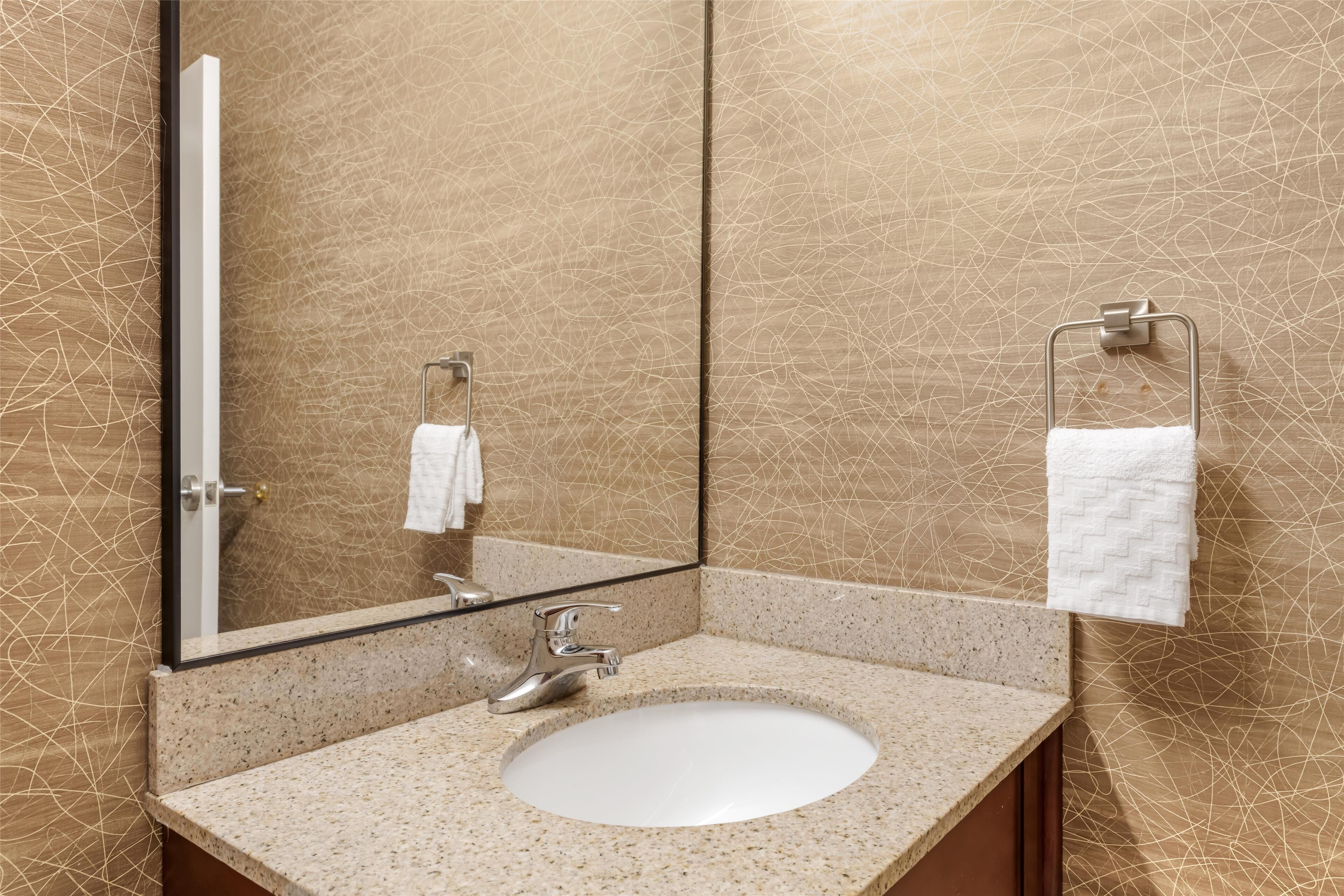 A bathroom with a granite countertop sink, a mirror, and a towel rack.