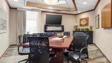 A conference room with a large table, black chairs, a flat-screen TV, and a decorative vase with flowers.