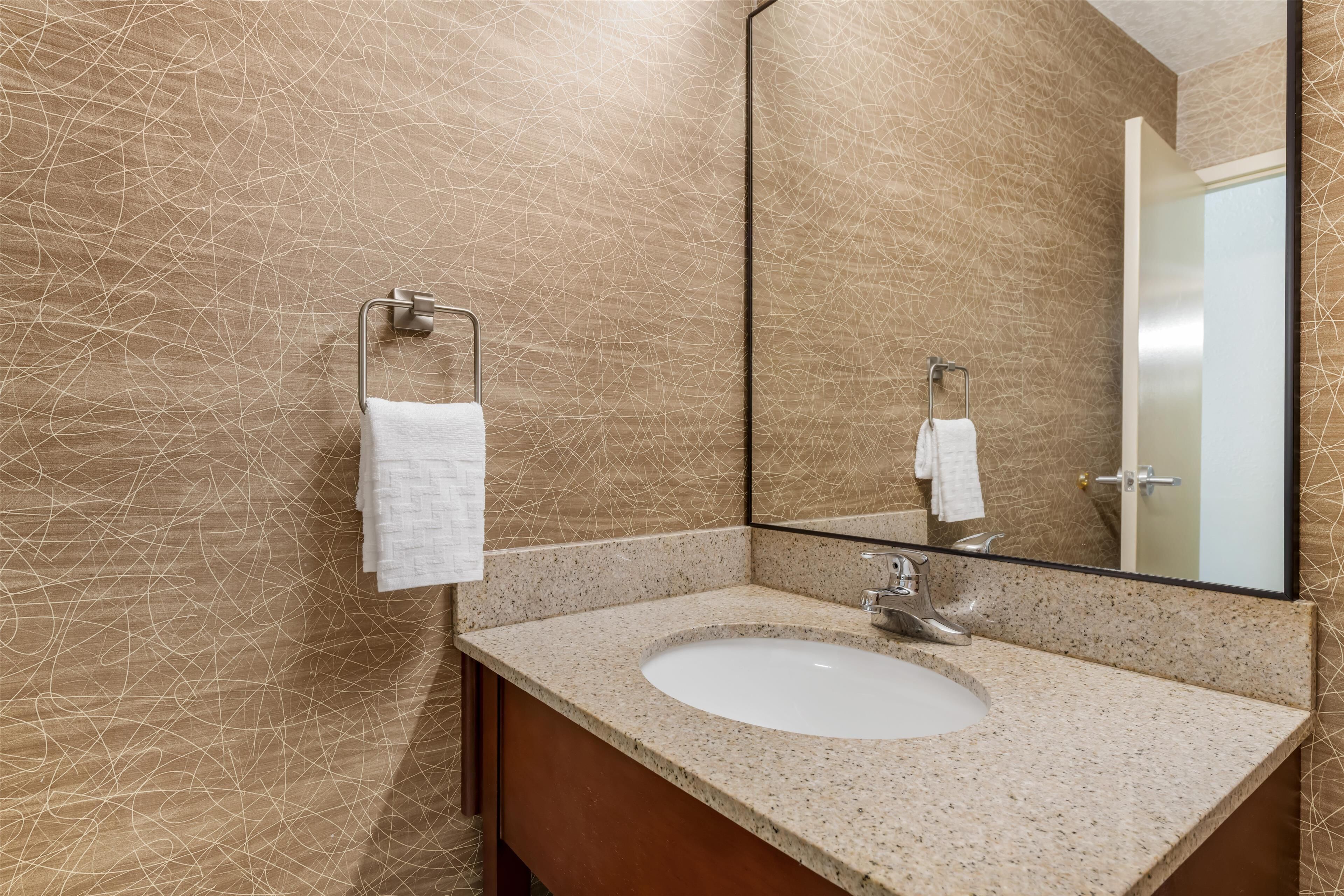 Une salle de bain avec un lavabo doté d’un plan de travail en granit, un grand miroir et un porte-serviettes.